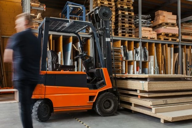 En man som står vid en röd truck som är lastad med plywood. I bakgrunden syns lagerhyllor.
